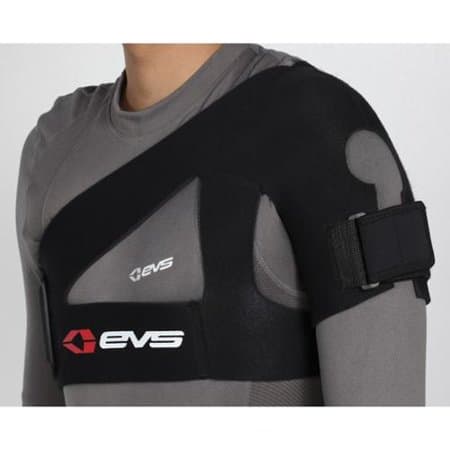 Black EVS SB02 shoulder support in size S, featuring a padded design, adjustable strap, and logo, worn over a gray long-sleeve shirt.