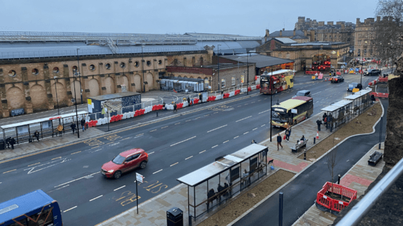 View of York Station area under construction, featuring traffic, bus stops, and barriers with historic buildings in the background.