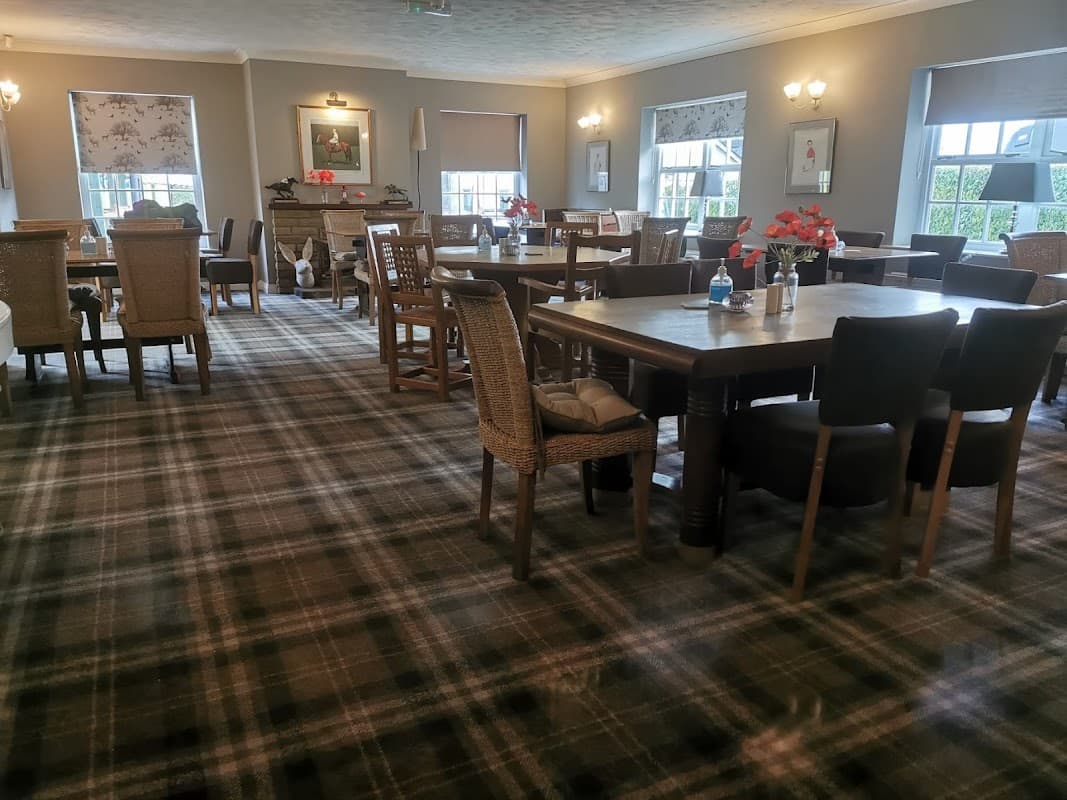 Cozy pub interior with wooden tables, wicker chairs, and a checkered carpet, adorned with floral centerpieces.
