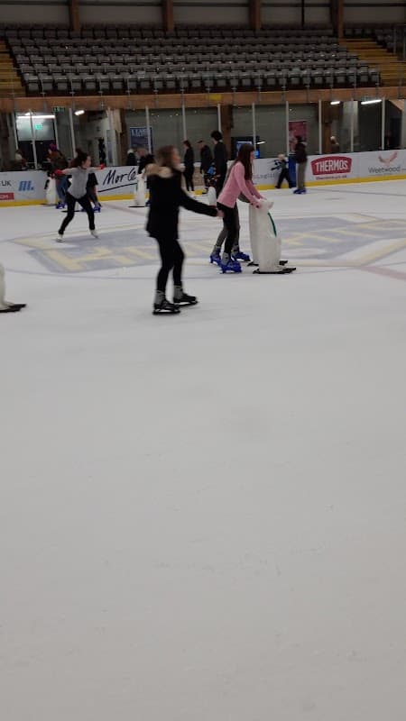 Skaters glide on ice at Elland Road's Park and Ride, with a rink backdrop and spectators in the stands.