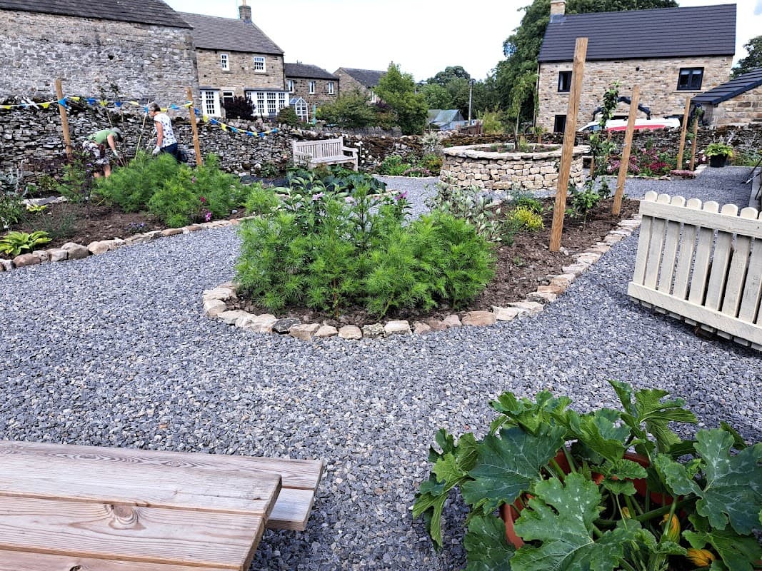 Lush community garden with gravel paths, stone walls, benches, and various plants in Bellerby, Yorkshire.