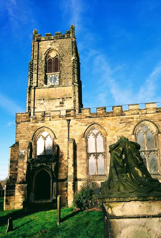 Historic stone church with a tall clock tower and arched windows, surrounded by green grass under a blue sky.