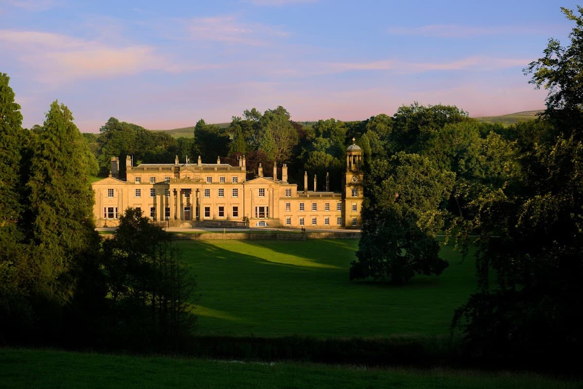 Elegant yellow stone hotel surrounded by lush greenery, with classical architecture and a serene landscape in Yorkshire.