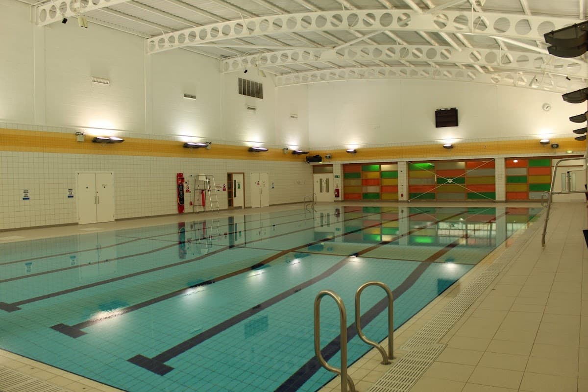 Indoor swimming pool with clear water, tiled walls, and colorful panels in the background. Brightly lit environment.