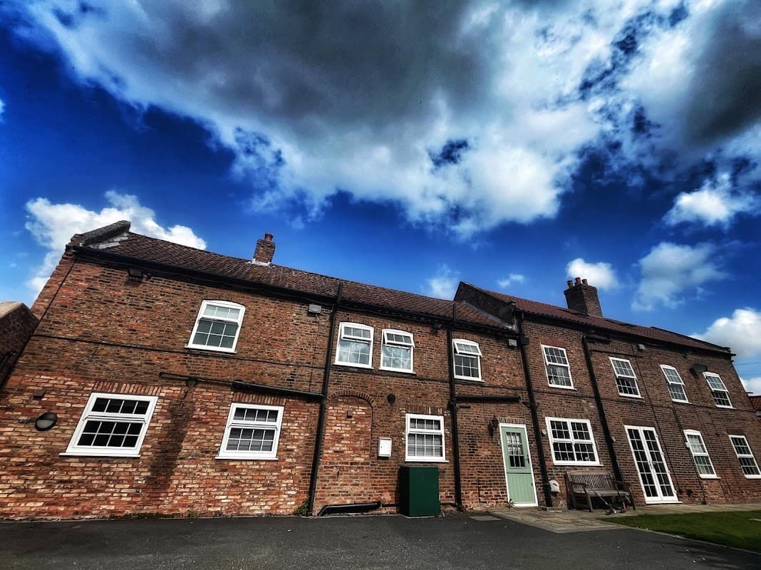 Red-brick guest house with multiple windows, green door, and a bench under a dramatic sky in Cawood, Yorkshire.