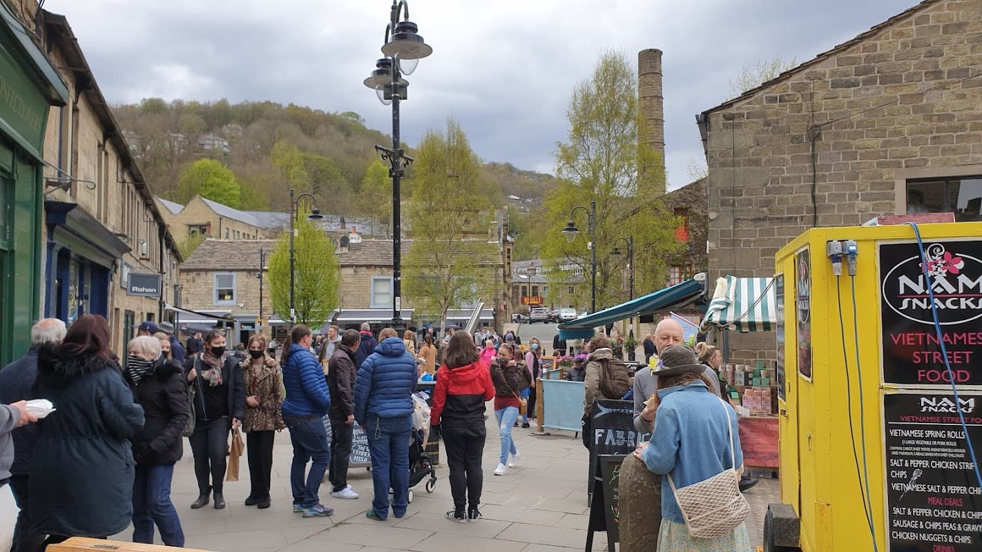 Busy street scene with people gathering near food stalls and shops, surrounded by trees and historic buildings.