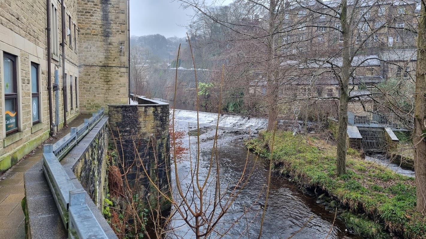 A view of a car park beside a river, with stone buildings and bare trees in a misty Yorkshire setting.
