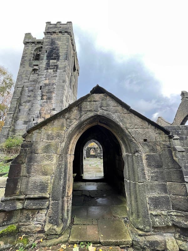 Archway leading to a stone structure with a tower, surrounded by greenery and a cloudy sky in Chiserley, Yorkshire.