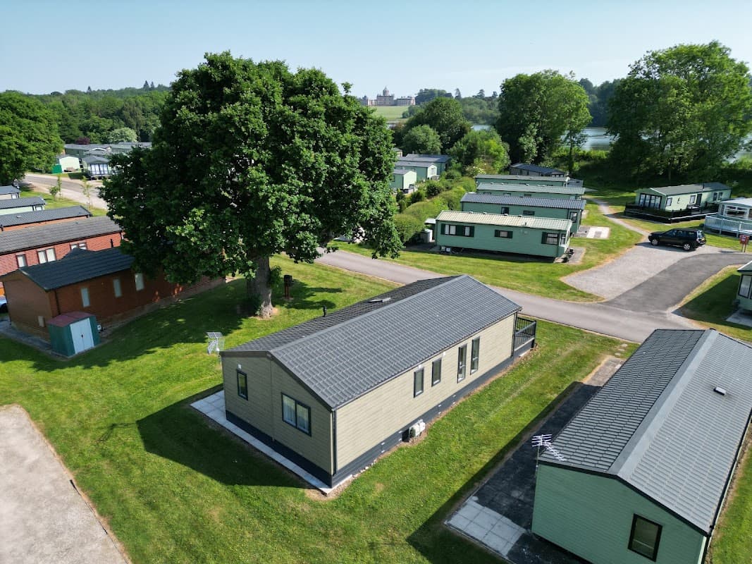 Lakeside holiday park with green caravans, lush trees, and a scenic view of the lake in Coneysthorpe, Yorkshire.