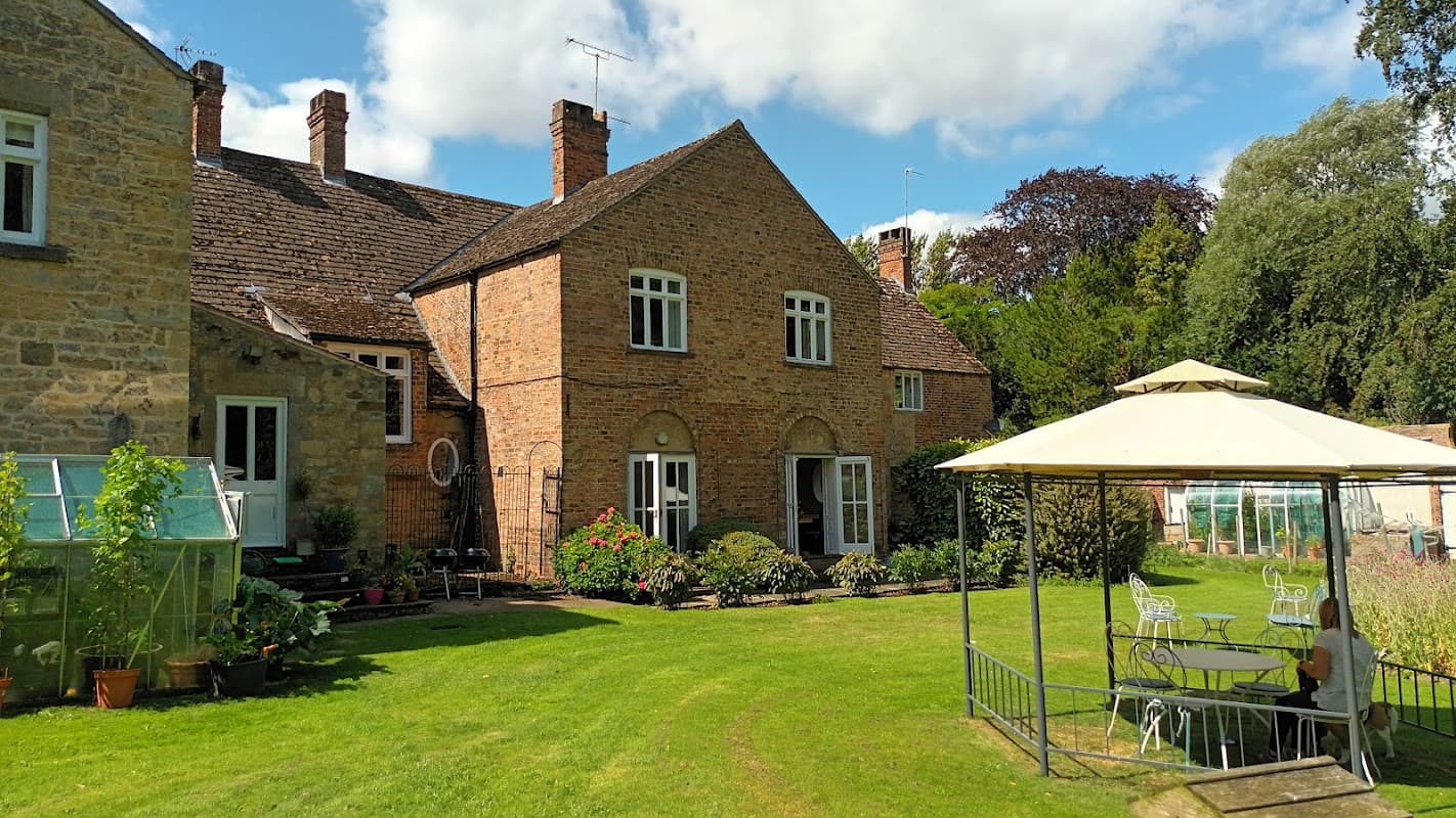 Newburgh House features a brick exterior, manicured lawn, garden plants, and a gazebo with seating in a serene setting.