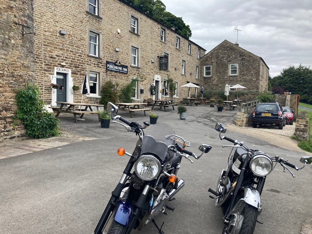 Two motorcycles parked in front of The Punch Bowl Inn, a stone building with outdoor seating and trees in Crackpot, Yorkshire.