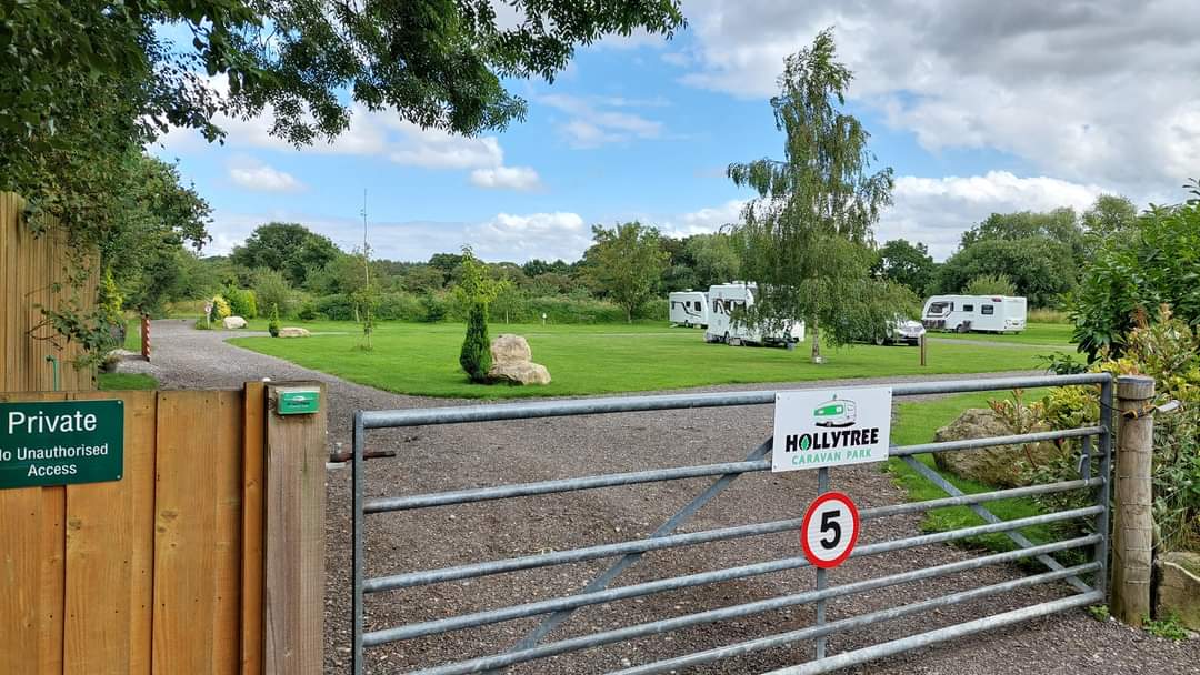 Green grass area with caravans, trees, and a gated entrance marked "Hollytree Caravan Park" in Dunnington, Yorkshire.