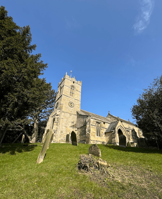 St Hilda's Church in Ellerburn, Yorkshire, features a stone tower, arched windows, and surrounding gravestones.