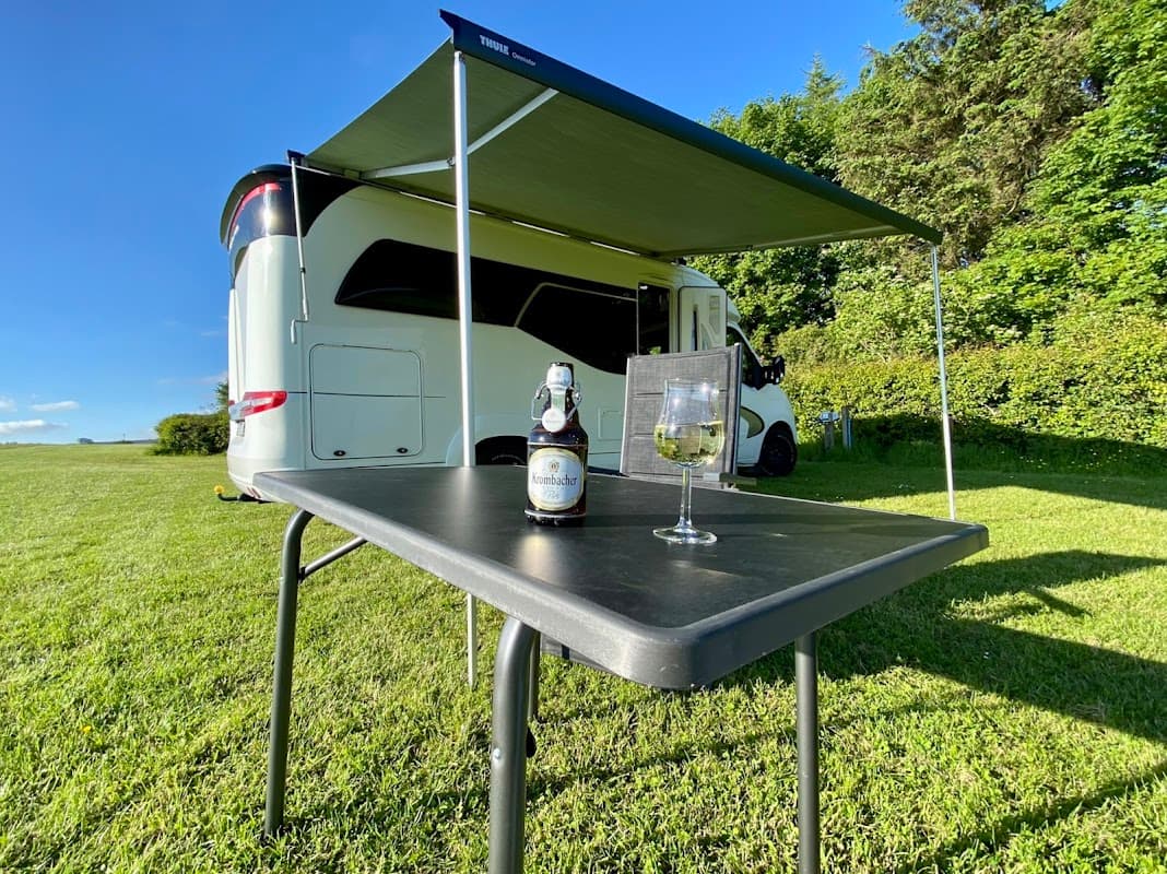 A caravan under a green awning with a table set for drinks, surrounded by lush grass and trees in Fadmoor, Yorkshire.