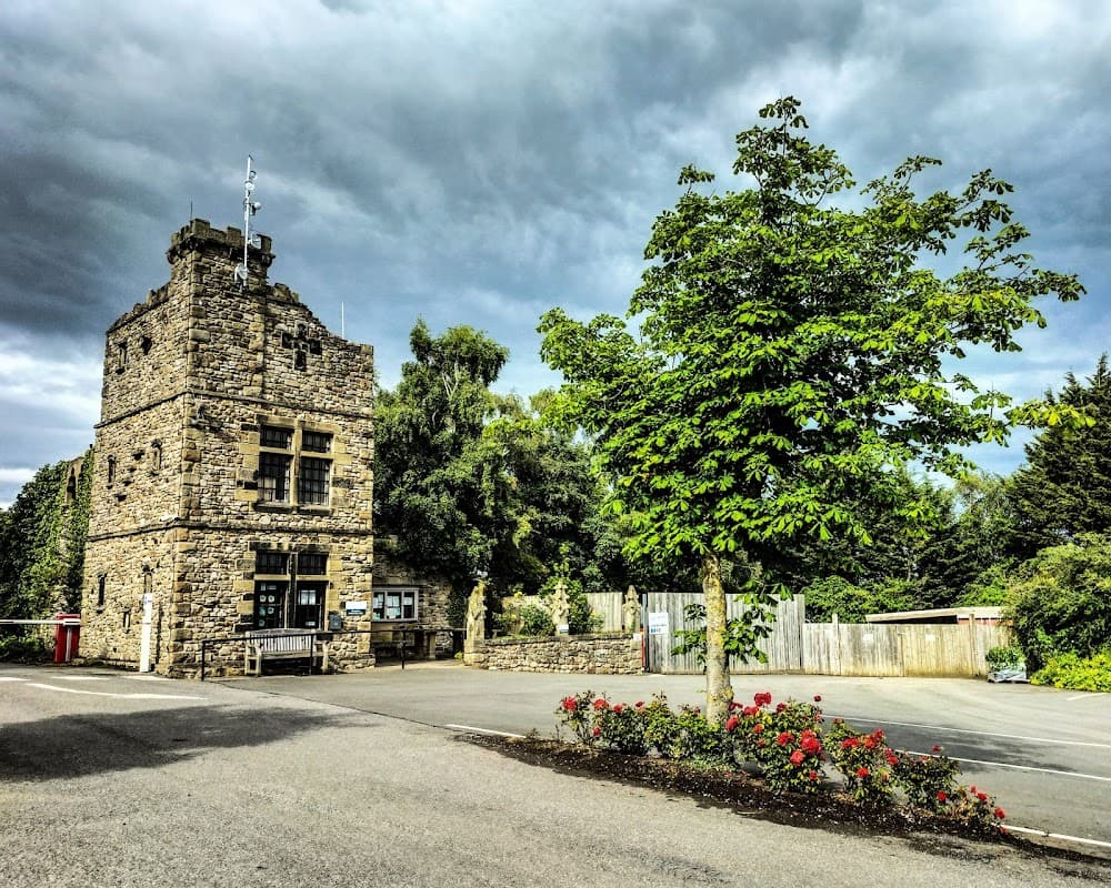 Stone building with a tower, surrounded by trees and flowers, under a cloudy sky at Akebar Park Golf Course.