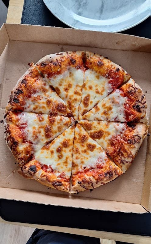 A freshly baked cheese pizza, sliced into eight pieces, in a cardboard pizza box.