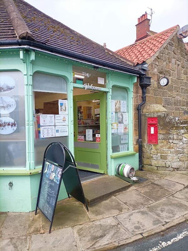 Green storefront of Thorpe Stores with a welcome sign, display windows, a blackboard menu, and a red post box nearby.