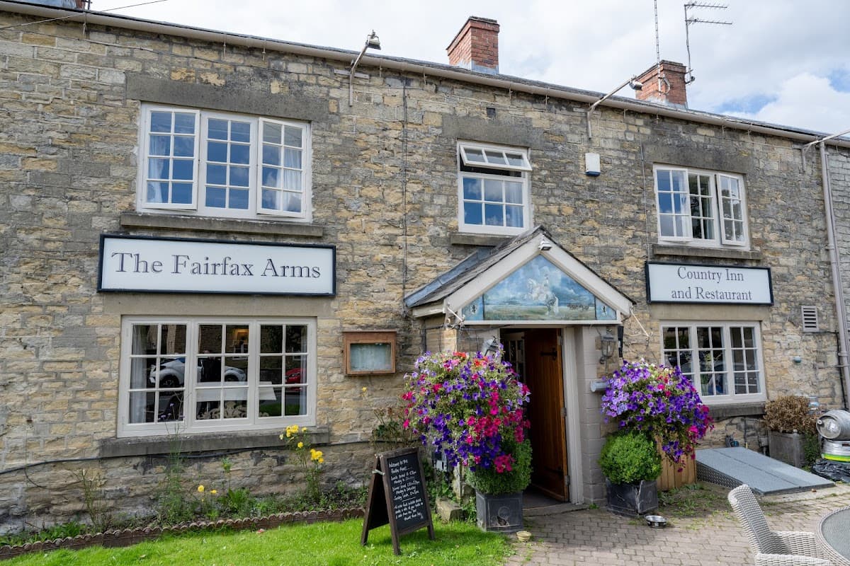Stone building with large windows, colorful flower baskets, and signs for "The Fairfax Arms" and "Country Inn and Restaurant."