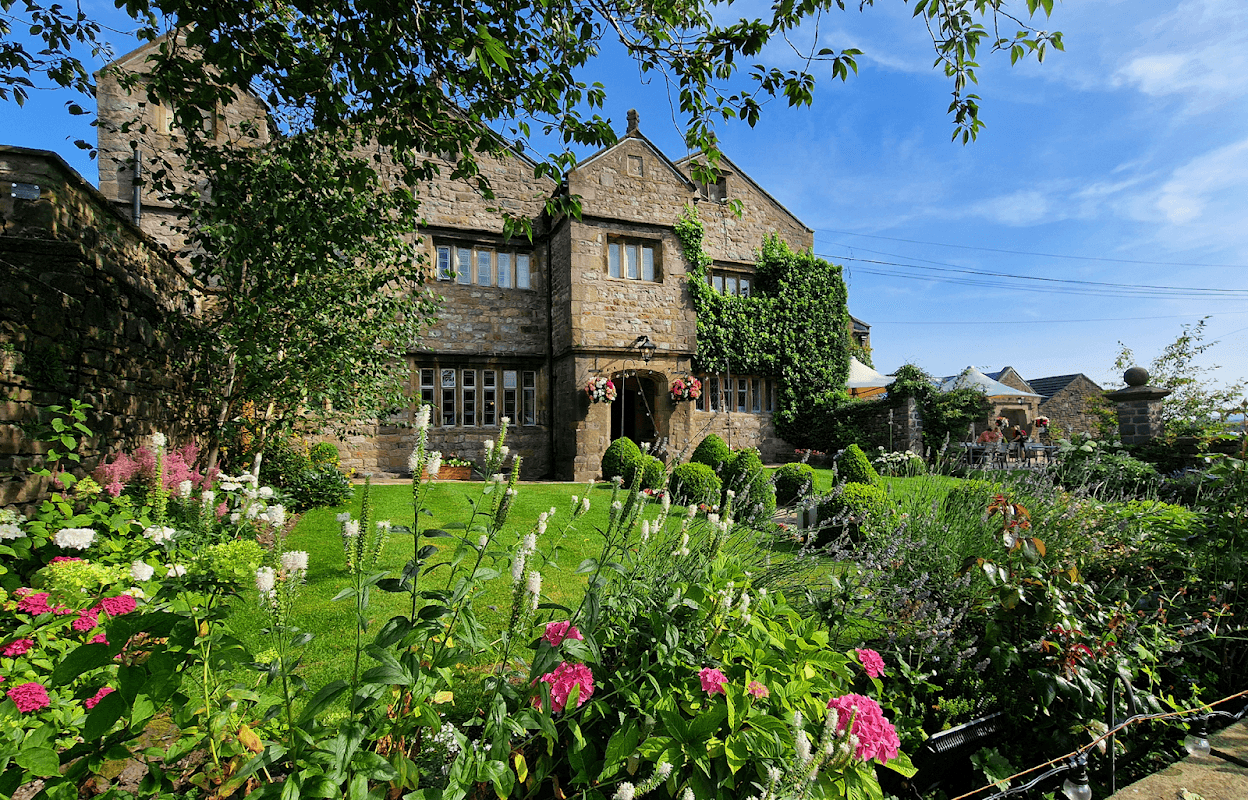 Historic Stirk House Hotel surrounded by lush gardens and colorful flowers under a clear blue sky.