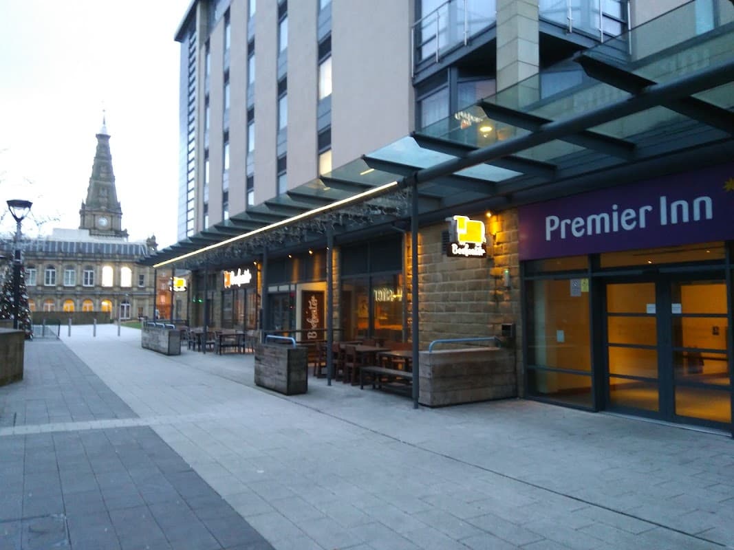 Broad Street Plaza features outdoor seating, modern architecture, and the Premier Inn sign, with a church tower in the background.