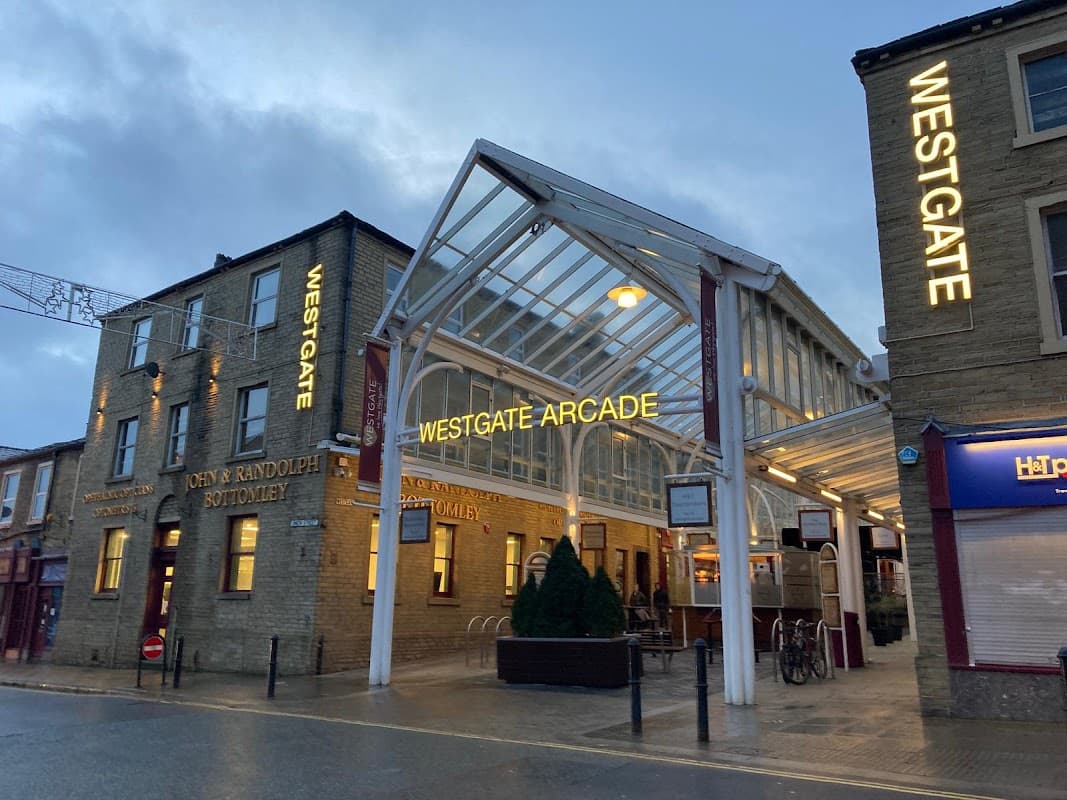 Westgate Arcade entrance featuring glass roof, illuminated signage, and surrounding brick buildings in Halifax, Yorkshire.