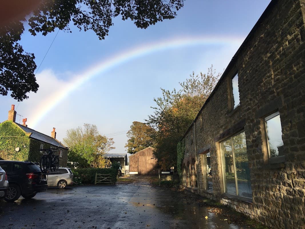 Murk Head Holiday Cottages with a rainbow arching over a stone building and lush greenery in Harwood Dale, Yorkshire.