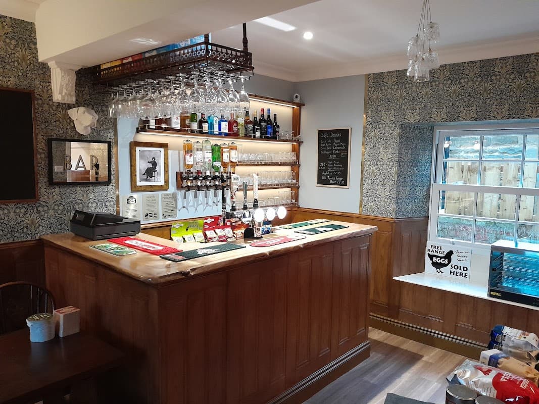 Cozy bar area with wooden counter, shelves of drinks, and a window overlooking a garden. Wallpaper adds character.