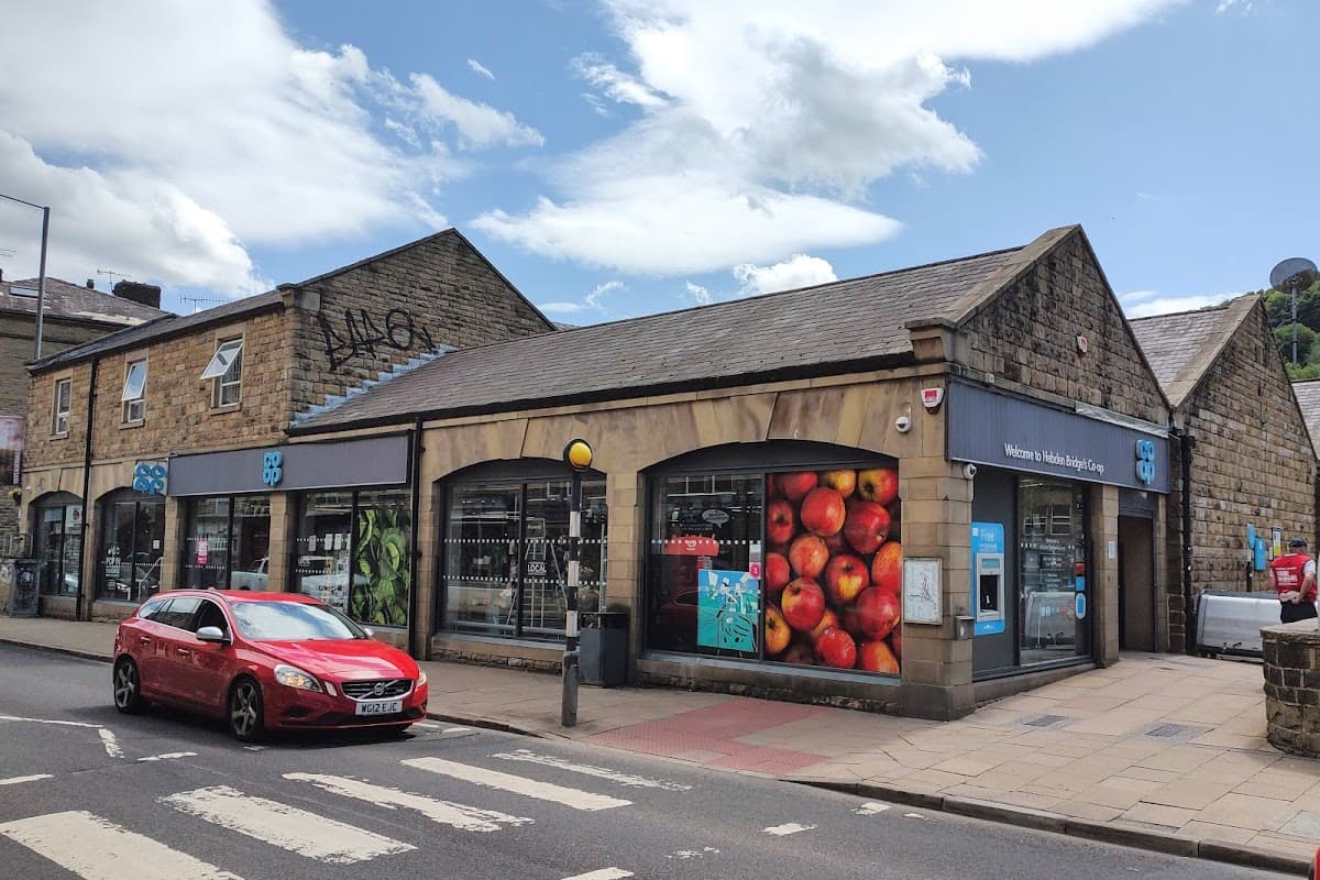 Co-op Food storefront in Hebden Bridge, featuring colorful apple display and a red car parked nearby.