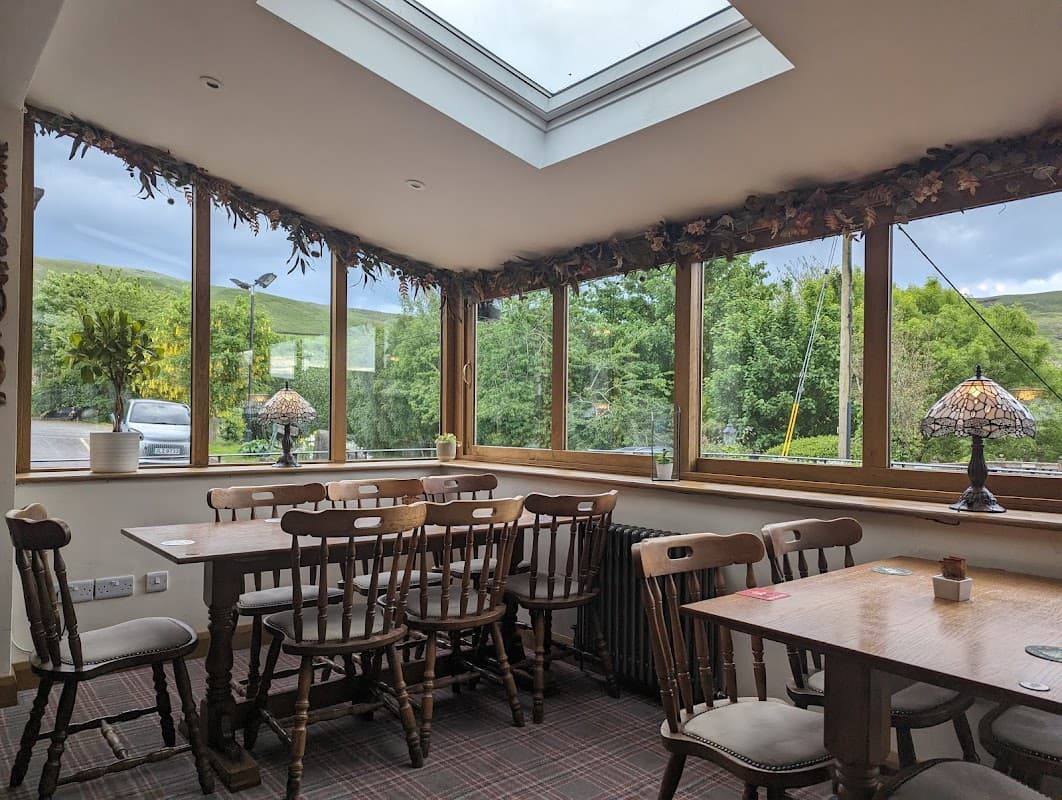 Cozy bar interior with wooden tables, chairs, and large windows overlooking lush greenery. Warm lighting and decor.