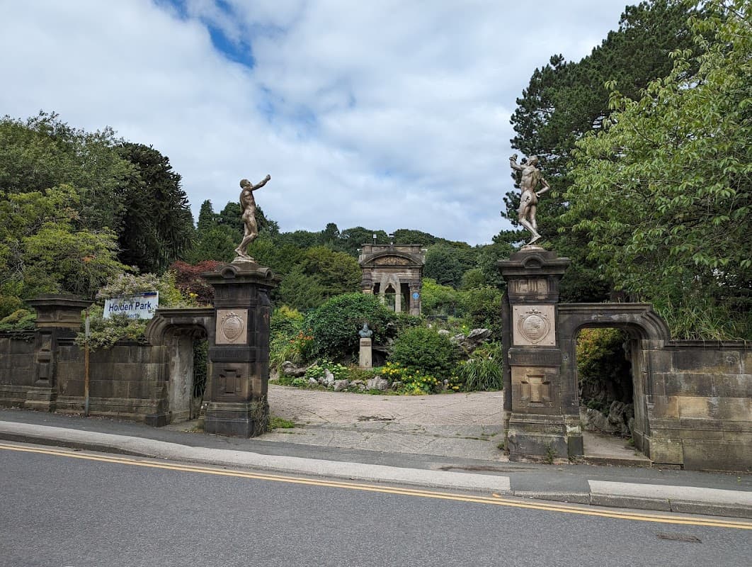 Entrance to Holden Park featuring stone gates, statues, and lush greenery under a cloudy sky.