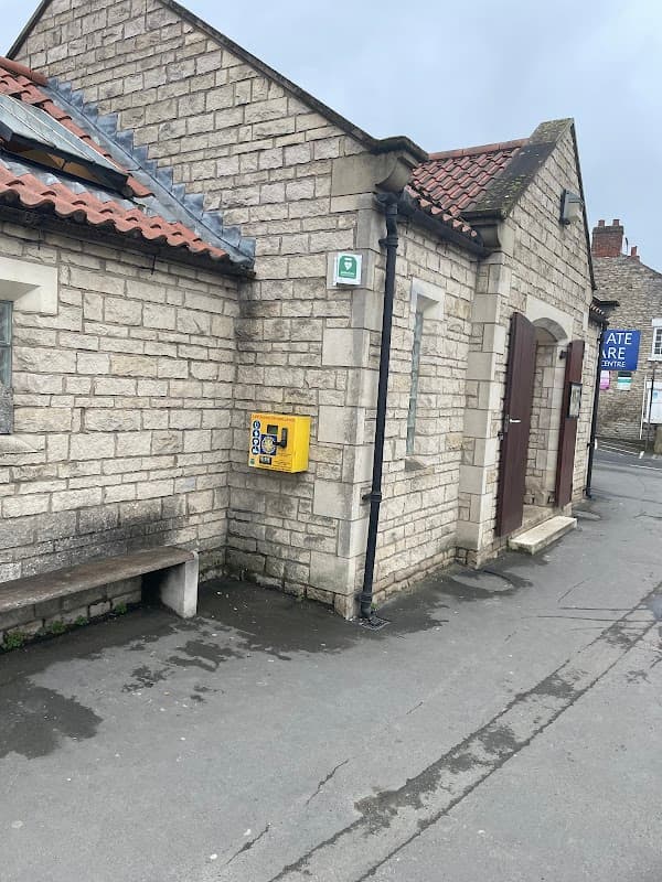 Eastgate car park toilets in Pickering, featuring stone walls, wooden doors, and a yellow emergency phone.