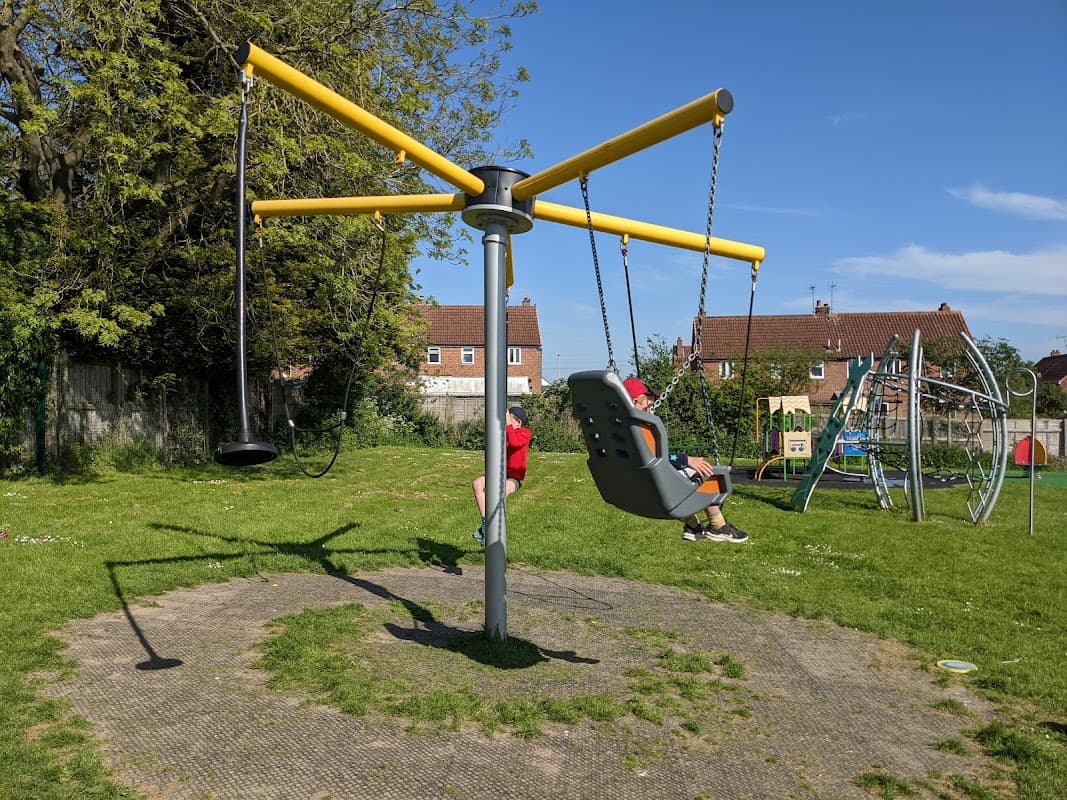 Bright playground with a large yellow swing set, green grass, and play equipment in the background under a clear blue sky.
