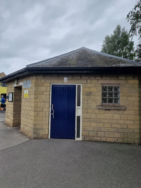 Public toilets in a stone building with a blue door, surrounded by a paved area and trees in Pickering, Yorkshire.