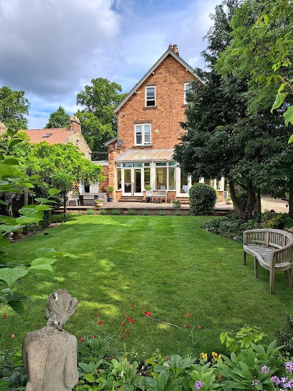 Victorian-style hotel with a conservatory, surrounded by a lush garden and greenery in Pickering, Yorkshire.