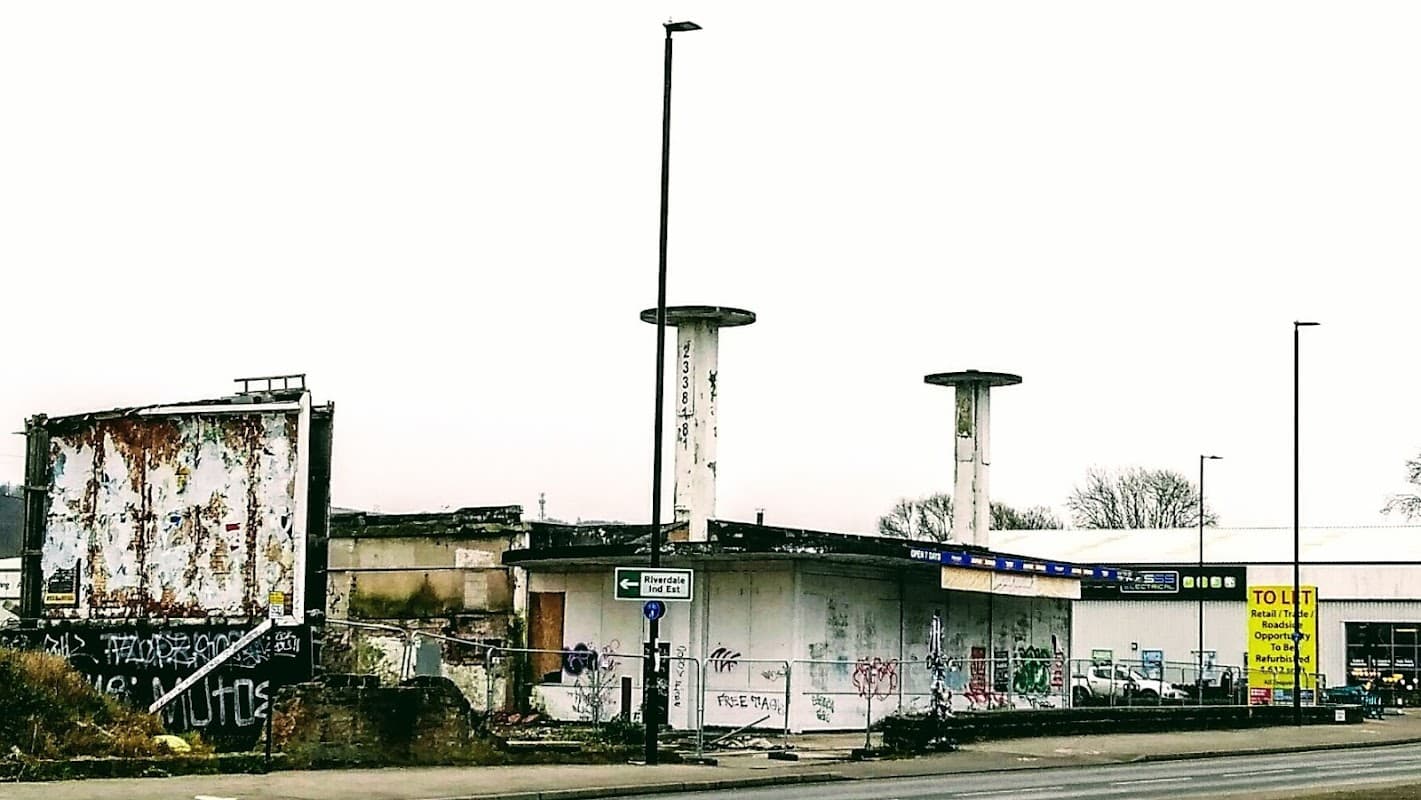 Abandoned car park with graffiti, large empty billboard, and two tall columns against a grey sky.