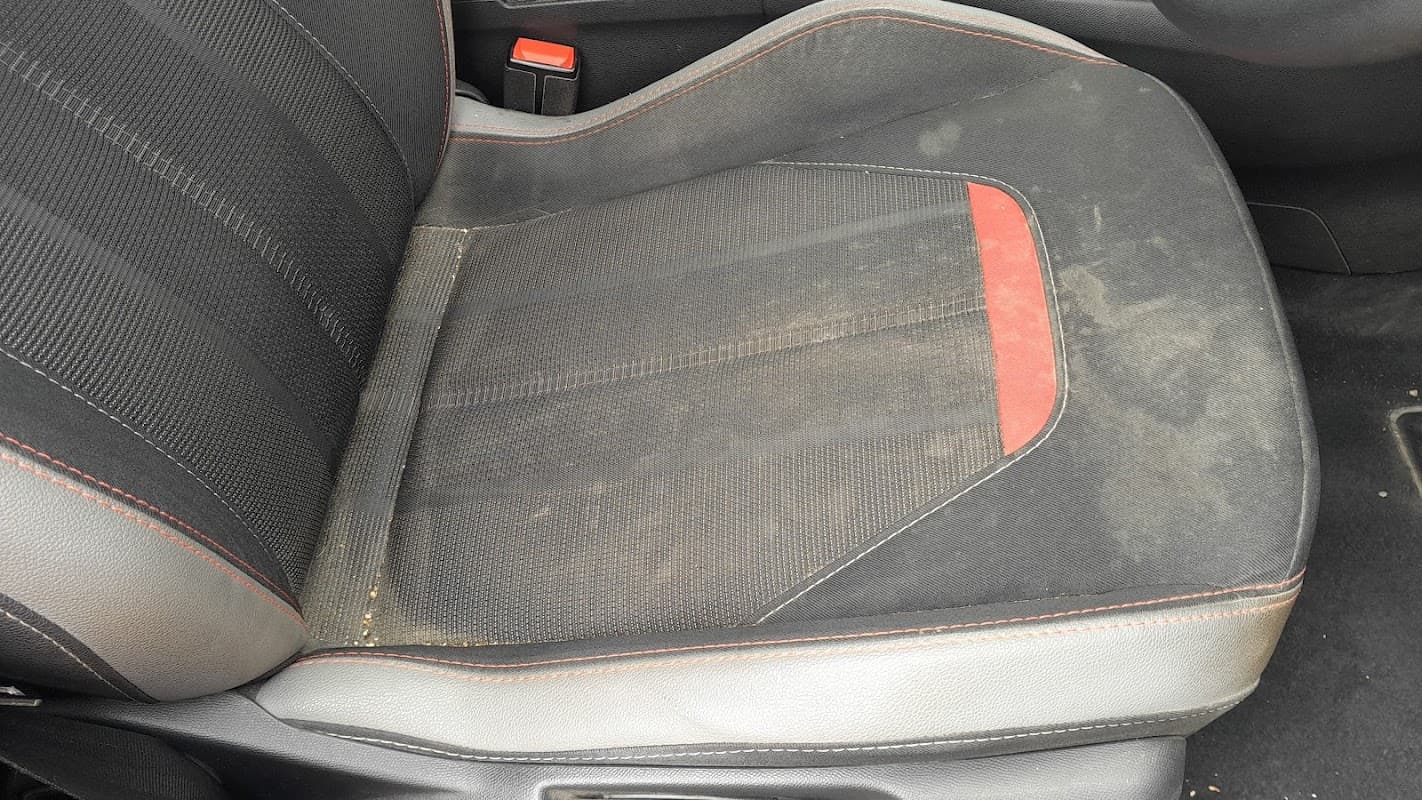 Dirty car seat with black fabric and red accents, showing dust and grime accumulation.