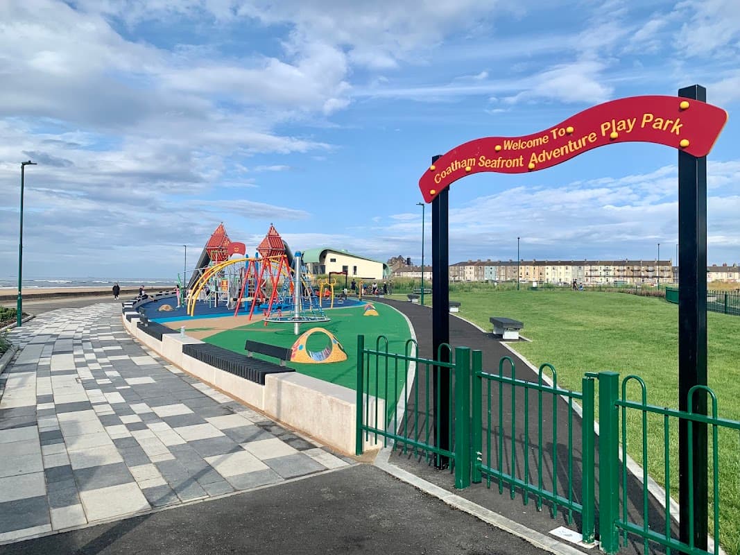 Colorful playground equipment with swings and climbing structures, surrounded by green grass and a scenic coastal view.