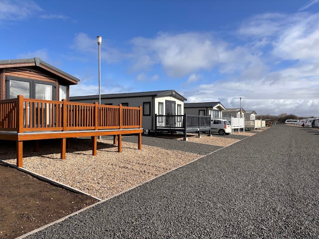 Modern caravans with wooden decks lined along a gravel path under a partly cloudy sky at Coatham Caravan Park.