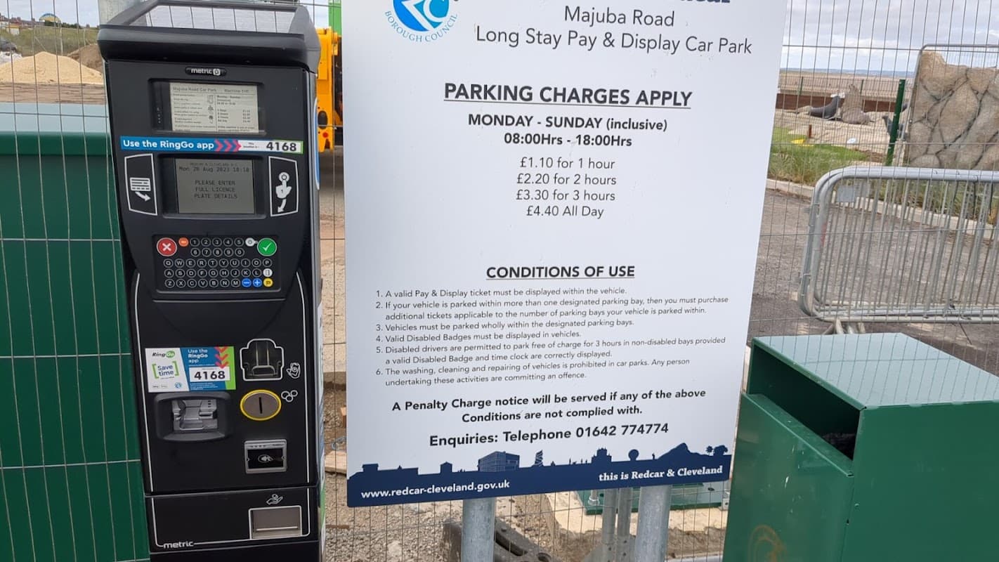 Pay & Display parking sign with rates and conditions, alongside a parking meter and car park entrance in Redcar.