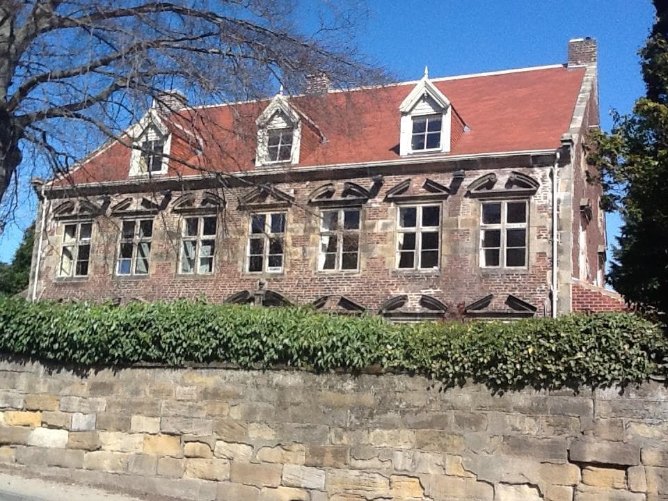 Historic brick building with a red roof, large windows, and stone wall, surrounded by greenery in Ruswarp, Yorkshire.