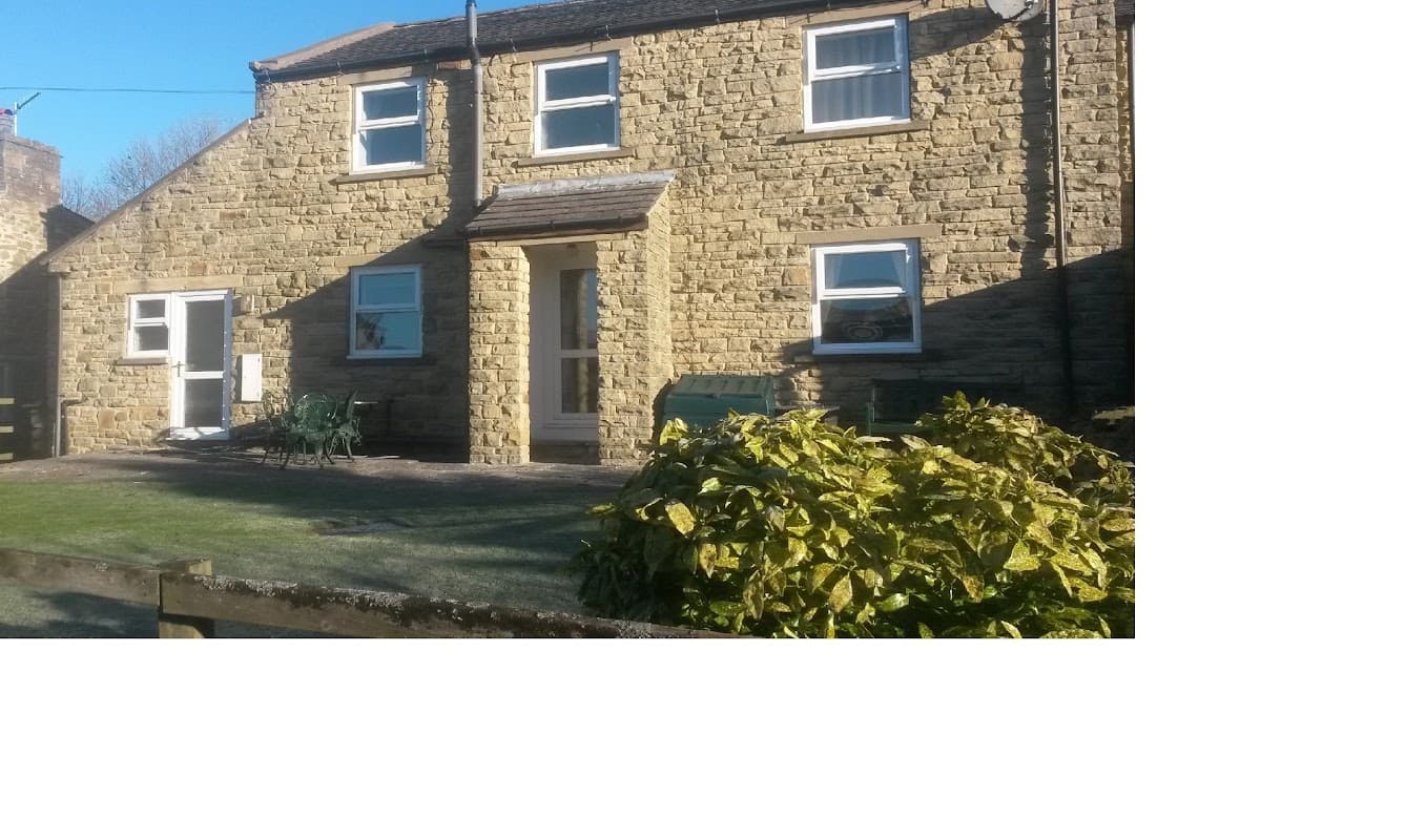 Wagtail Cottage features a stone exterior, a front door, and green seating in a garden setting in Sedbusk, Yorkshire.