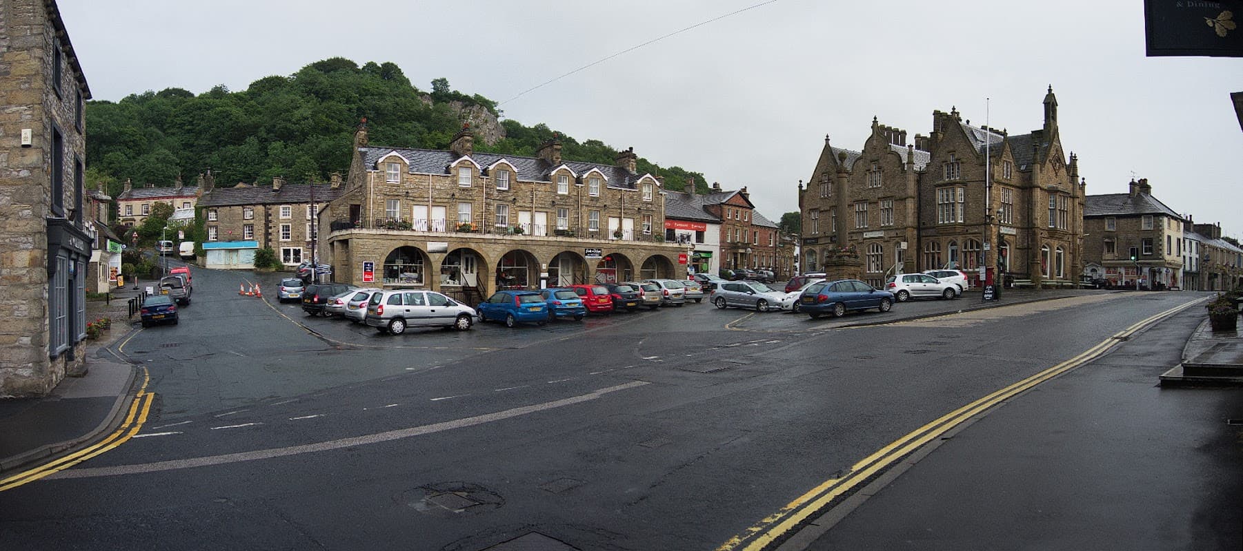 Pay & Display parking area in Settle, Yorkshire, with stone buildings, parked cars, and a hill in the background.
