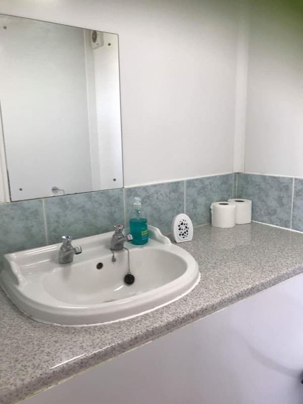 Clean sink area with a mirror, soap dispenser, and toilet paper rolls on a countertop.