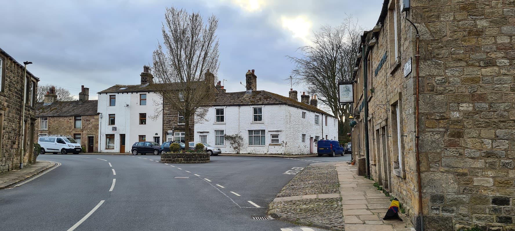 Main St Car Park in Skipton, featuring stone buildings, a roundabout, and parked cars under a cloudy sky.