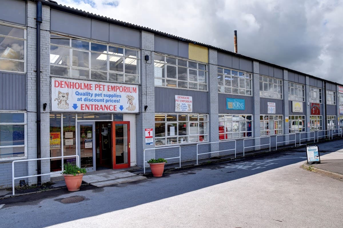 Denholme Pet Emporium storefront with large windows, colorful signage, and potted plants at the entrance.