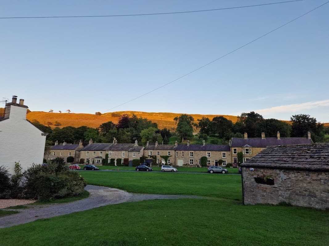 Charming hotel with stone buildings, green lawn, and a hillside bathed in warm sunset light in West Burton, Yorkshire.