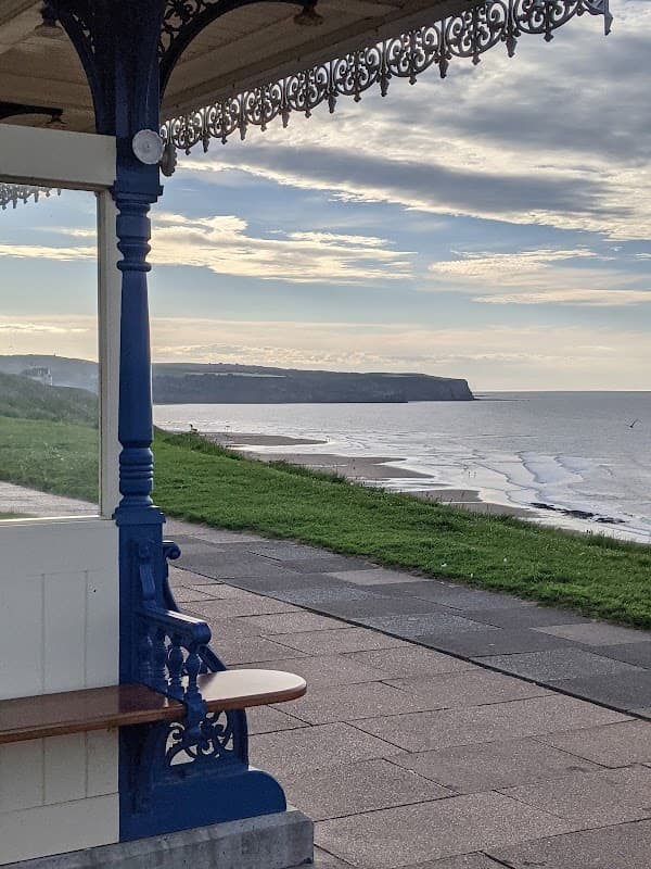 View from a seaside shelter overlooking the beach, cliffs, and calm sea under a cloudy sky in Whitby, Yorkshire.