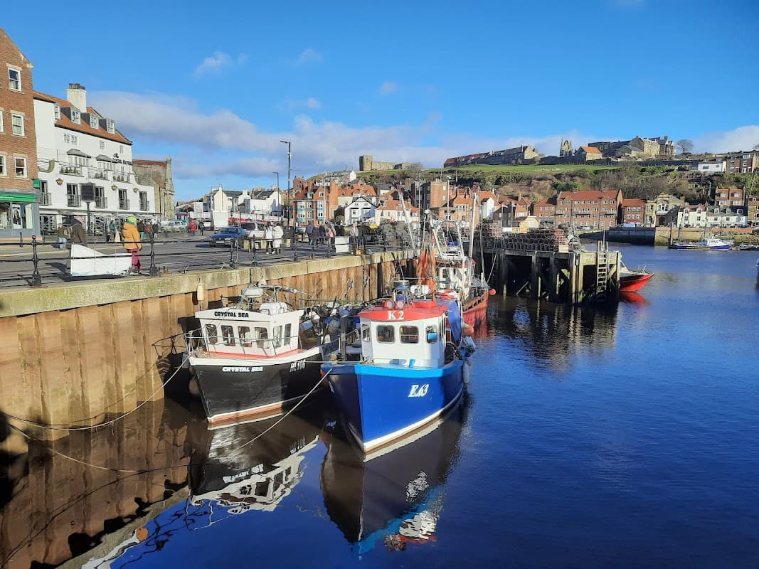 Colorful fishing boats docked in a calm harbor, with historic buildings and a hillside castle in the background.