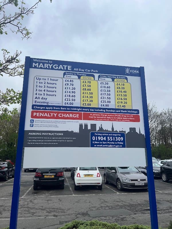 Sign displaying parking rates and instructions at Marygate Car Park, York, with cars parked in the background.
