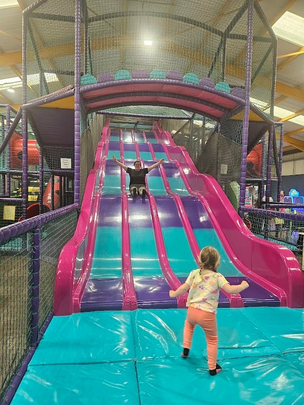Colorful indoor slide with children playing; one slides down while another stands at the bottom, excited.